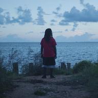 A scene from a film, with a woman peering out into the horizon.