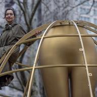 A woman sitting next to a sculpture being installed.
