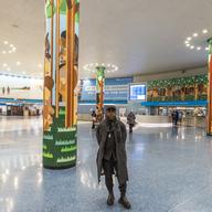 A man standing in a train station, surrounded by green, leafy art.