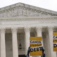 Two signs saying 'cancel student debt' are held up in front of the Supreme Court