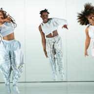 Three women dressed in white outfits are jumping in the air as they dance hip-hop.