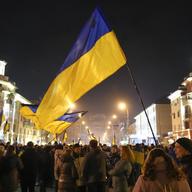 A Ukrainian flag is waved above a crowd at night 