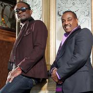 Two men standing against a wall.
