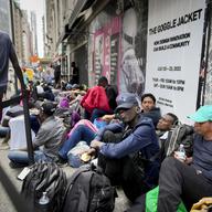 Migrants sit in a queue outside of The Roosevelt Hotel that is being used by the city as temporary housing, Monday, July 31, 2023, in New York.