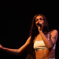 Rapper Heather Hills is holding a microphone to her mouth while on stage looking out toward the audience. 