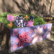 A raised garden bed at St. Nicholas Miracle Garden in Central Harlem. The box is painted with pink and purple flowers. There is a sign in the garden box that reads 'love is in the soil.' 