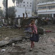 A Palestinian girl carries a blankets as she walks past the site of a deadly explosion at al-Ahli hospital, in Gaza City, Wednesday, Oct. 18, 2023.