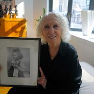 Doris Schechter, 85, poses in her Midtown apartment with the photo of her arrival as a 6-year-old on the Henry Gibbins.