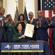 This image provided by the Office of The Governor, shows New York Gov. Kathy Hochul, seated center, after she signed a bill, in New York, Tuesday, Dec. 19, 2023, to create a reparations commission.