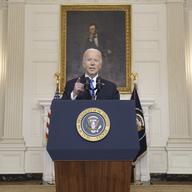 Biden stands at a podium with the presidential seal in front of a portrait of Lincoln.