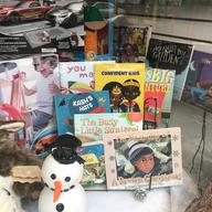 The front window of Grandma's Place, a children's book and toy store in Central Harlem, featuring books with various titles, including 'I'm Dreaming of a Brown Christmas,' and stuffed animals.