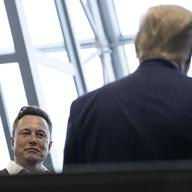 Elon Musk looks a Donald Trump, whose back is turned to the camera.
