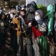 People hold their ground near a main gate at Columbia University in New York, Tuesday, April 30, 2024, as New York City police officers move to clear the area after a building was taken over by protes