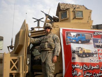 Wilkens standing on a vehicle used for missions. Beside him is a banner depicting dumptrucks used for enemy rocket launches.