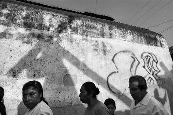 Donna De Cesare. Jocotenango, Guatemala 2001. A Holy Week procession passes village walls marked with the graffiti of the gang that dominates the zone. 