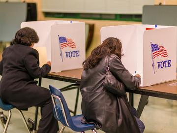 two women sitting at a table each working in her own voting booth