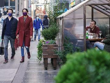 Two people wearing masks past by a shelter where diners are eating as part of outdoor dining at a restaurant in Manhattan. 