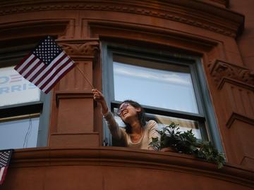 A woman waves an American flag out of her window.