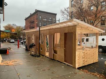 A man constructs a door to an outdoor dining shelter in Brooklyn.