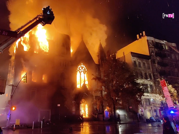 Fire rips through a church with firefighters on a crane above the church spraying water.