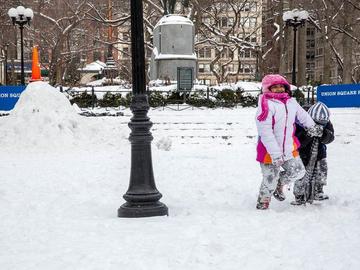 Two little kids in snow suits throw snow up in the air.