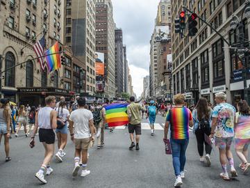People holding Pride flags and dressed in rainbow colors march down the center of the street in New York.