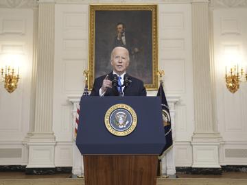 Biden stands at a podium with the presidential seal in front of a portrait of Lincoln.