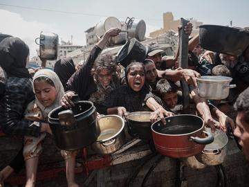 Palestinians, including children gather with cooking pots to receive hot meals distributed by a charitable organization in the Al-Ansar area of western Gaza City on August 1, 2025.
