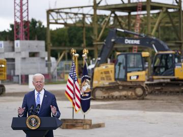 Biden stands in front of a construction site with a frame of a building behind him.