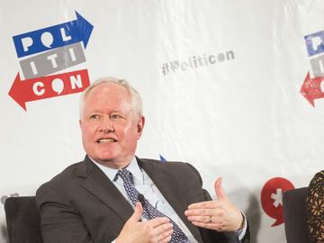 Bill Kristol, wearing a suit, sits in an arm chair on a panel discussion stage.