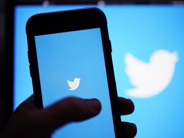A hand holds up a phone screen featuring the twitter logo.