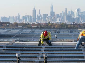 Framed by the Manhattan skyline, electricians with IBEW Local 3 install solar panels on top of the Terminal B garage at LaGuardia Airport, Nov. 9, 2021, in the Queens borough of New York. 