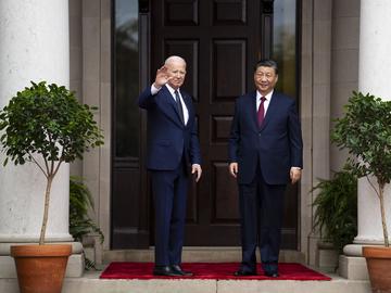Biden stands on the left waving , Jinping stands to the right with his arms at his sides