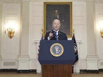 Biden stands at a podium with the presidential seal in front of a portrait of Lincoln.