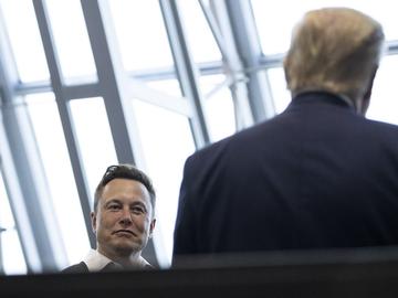 Elon Musk looks a Donald Trump, whose back is turned to the camera.