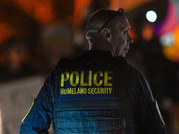A Department of Homeland Security agent stands guard as protesters demonstrate against recent raids conducted by the US Immigration and Customs Enforcement (ICE) outside the DHS office in Charlotte, N