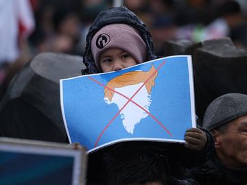 People, including a boy holding a placard that shows Greenland with the orange hair of U.S. President Donald Trump and Xed out, gather to march in protest against U.S. President Donald Trump.