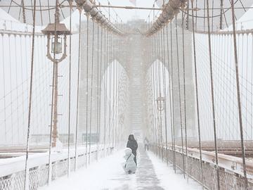 People walk along the Brooklyn Bridge as snow falls during a blizzard on February 23, 2026 in New York City.