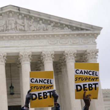 Two signs saying 'cancel student debt' are held up in front of the Supreme Court