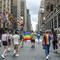 People holding Pride flags and dressed in rainbow colors march down the center of the street in New York.