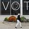 Woman walks past windows with 'Vote' written across them. 