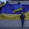 Man with Ukrainian flag stands in front of larger flag draped over concrete wall