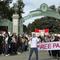 Two students hold a banner that says 'Free Palestine' in front of a green mental archway, with more people gathered in the background