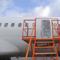 An orange ladder leads up to the side of a plane with the exit door missing, covered in plastic