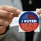 A election volunteer offers voters an 'I Voted' sticker after casting their ballot on Super Tuesday, at the Ranchito Elementary School polling station in the Panorama City section of Los Angeles, Tues