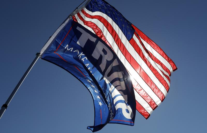 A supporter of Republican presidential candidate Donald Trump holds the American flag and a Trump campaign flag outside a campaign stop by Democratic presidential candidate Hillary Clinton at Wayne St