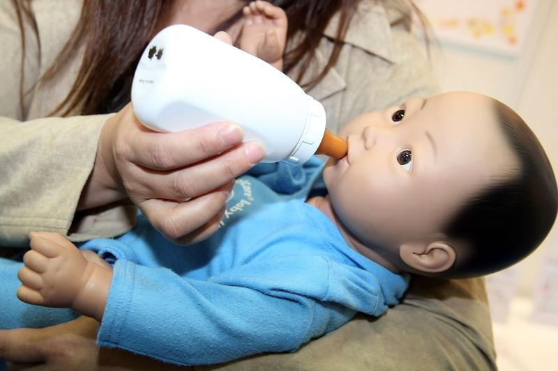 A woman holds the child-care simulation robot 'My Baby 2' by Realityworks during the 2007 International Robot Exhibition at Tokyo Big Site on November 28, 2007 in Tokyo, Japan.
