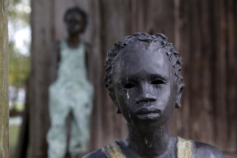 This July 14, 2017 photo shows two of the statues spread throughout the grounds, titled "Children of Whitney" by Woodrow Nash, in front of one of the slave cabins at the Whitney Plantation in La.