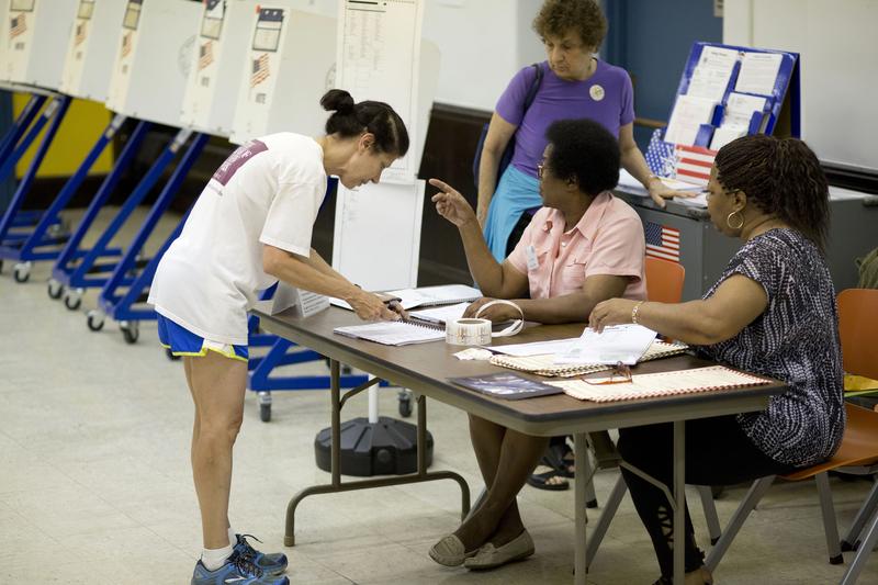 An unidentified voter, left, signs in to vote in the Democratic primary, Tuesday, Sept. 12, 2017, in Brooklyn.