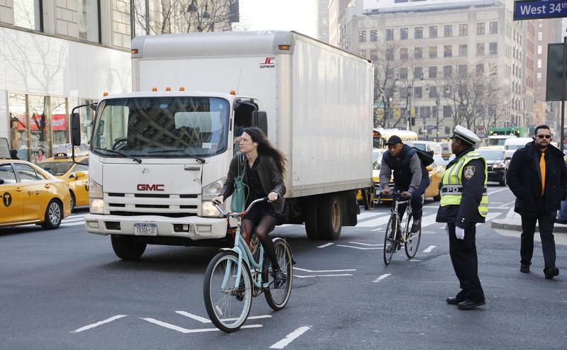 A cyclist wearing earbuds rides in a bike lane as a truck passes her, Wednesday, March 9, 2016 in New York.